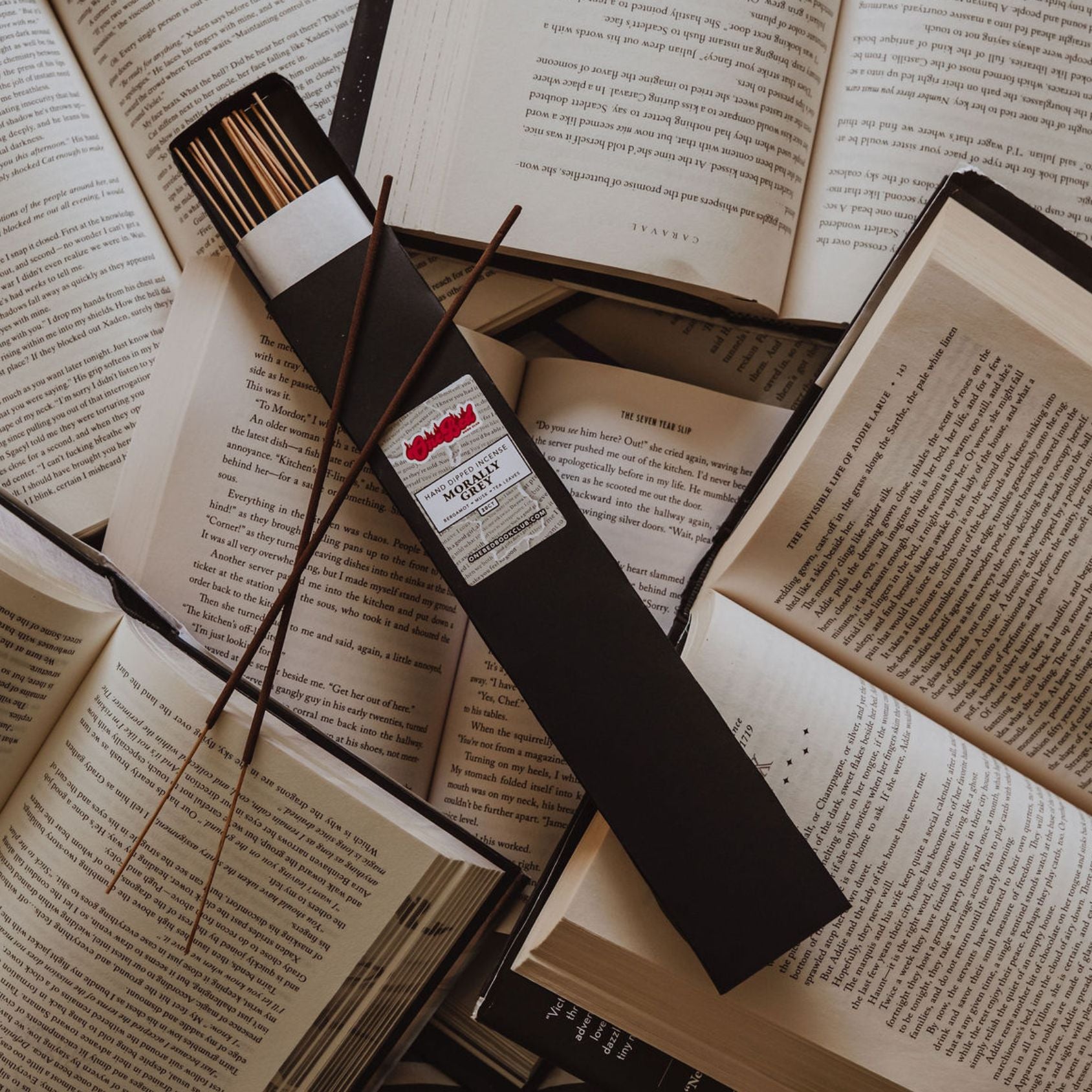 Angled shot showing incense bundle on top of book stacks with visible spicy book titles.