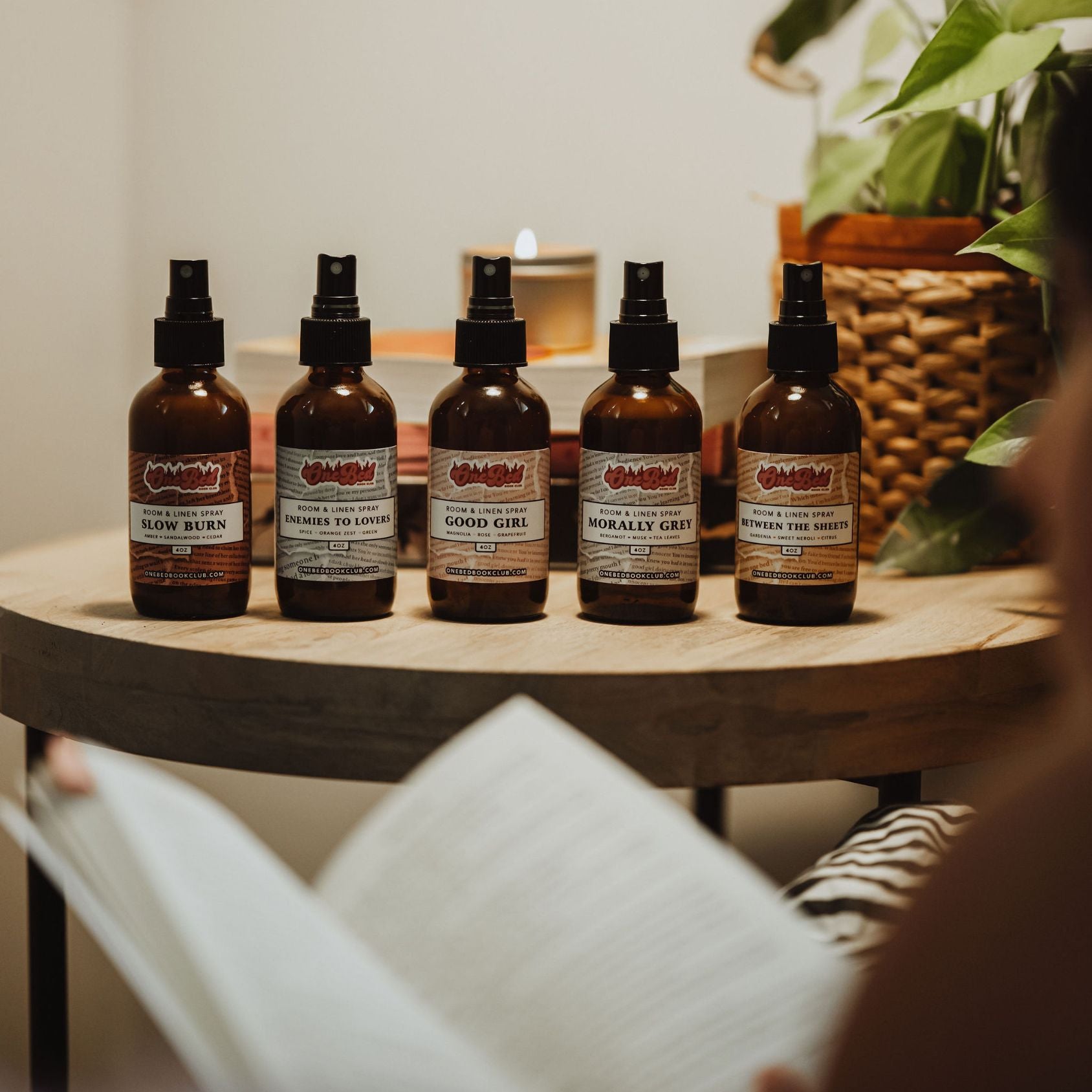Five bottles of One Bed Room Spray lined up against a book backdrop, showing scent labels.