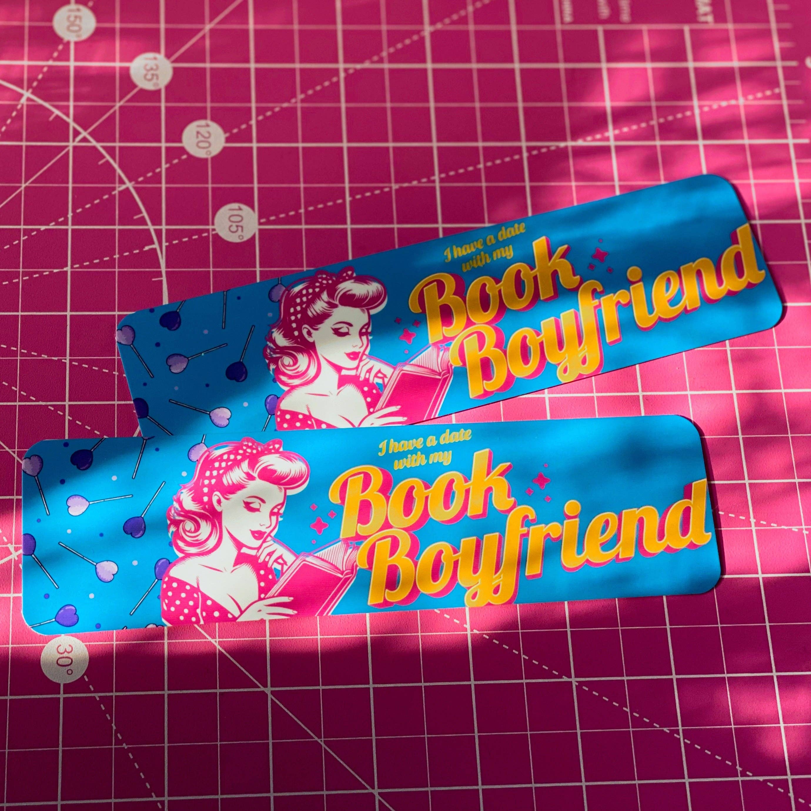 Two 'Book Boyfriend' bookmarks on a pink grid background