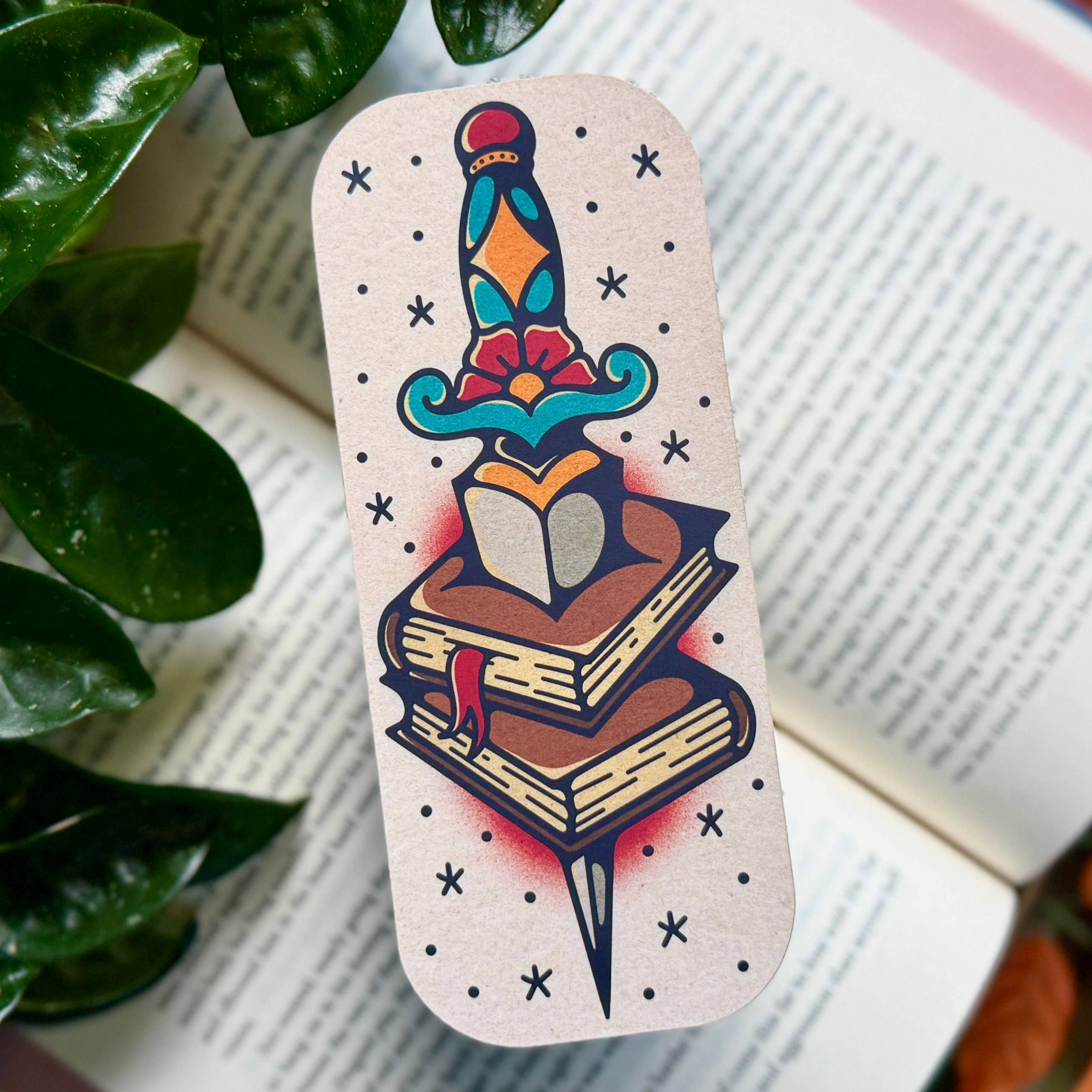 Bookmark with dagger, flower, and stack of books in bold colors