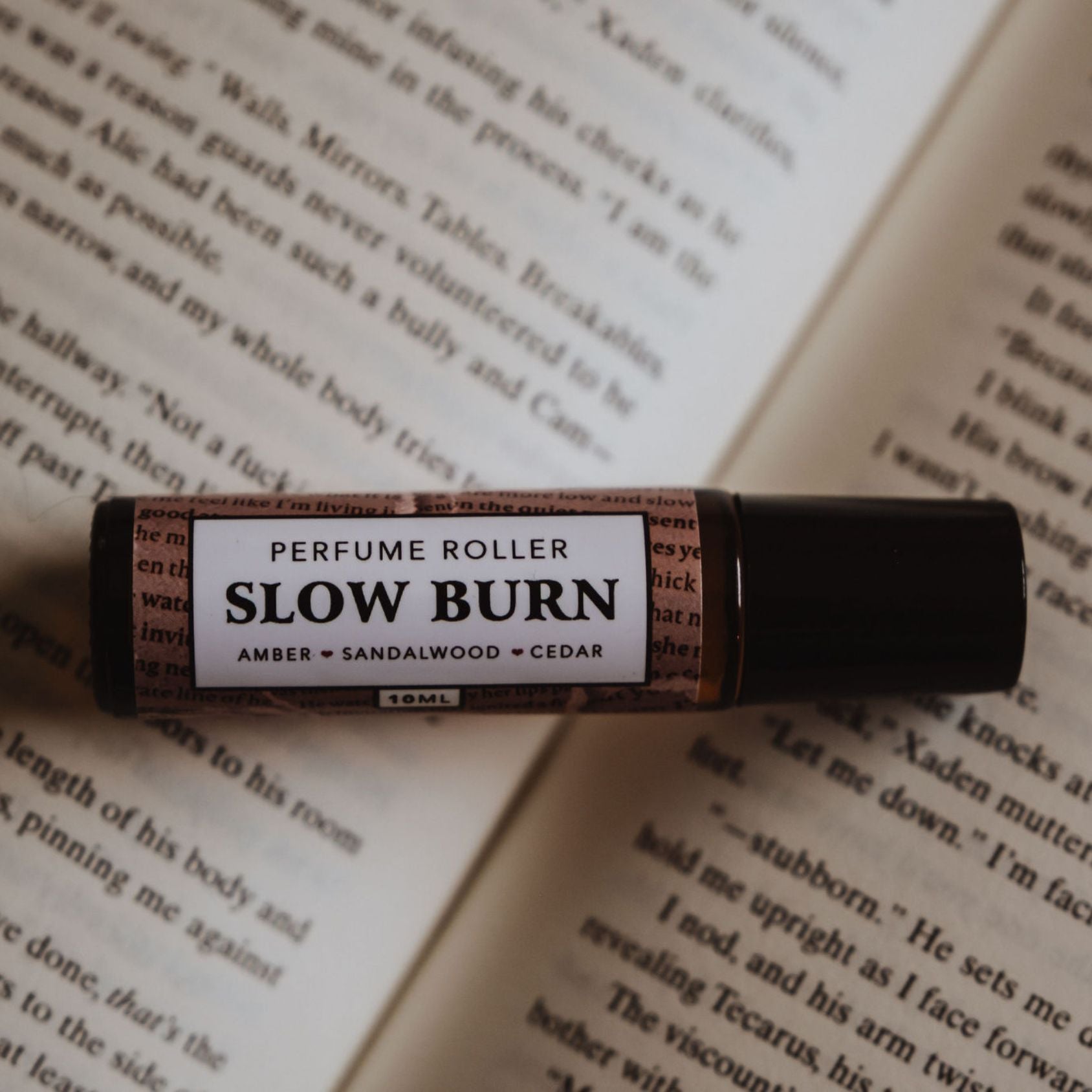 Flatlay of “Slow Burn” roller perfume bottle resting on open book pages.