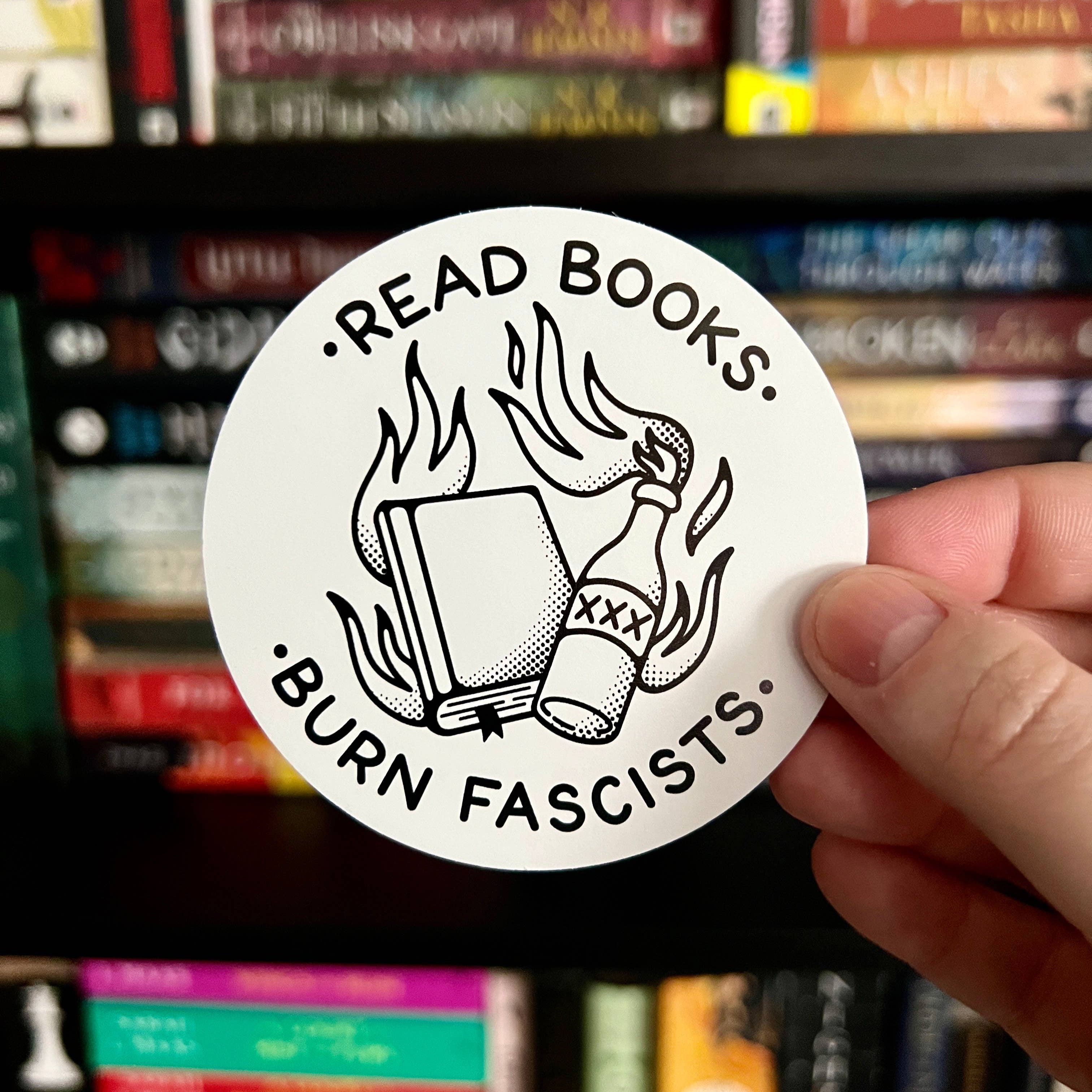 Black-and-white sticker with book and flames that reads “Read Books. Burn Fascists.”